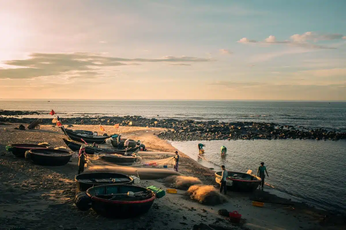 Plage de sable blanc au coucher de soleil avec pêcheurs et village côtier authentique en arrière-plan