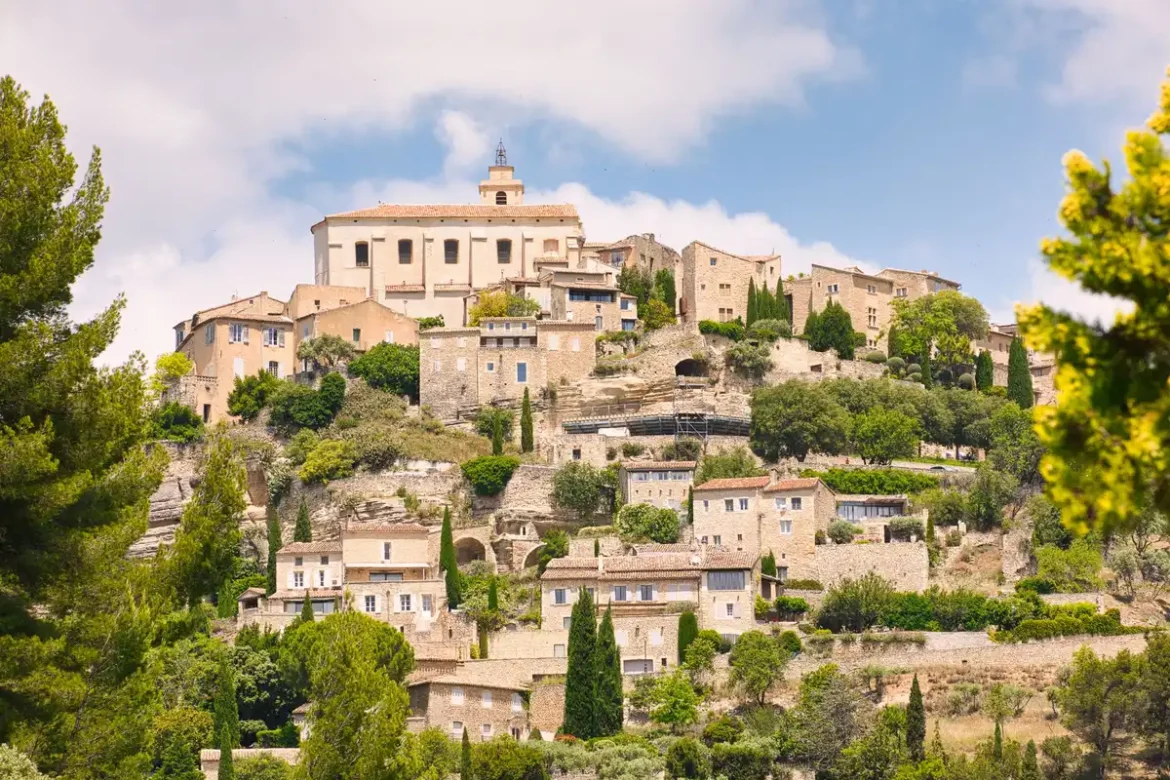 Vue aérienne d'un village provençal aux toits de tuiles rouges perché sur une falaise rocheuse, avec champs d'oliviers à
