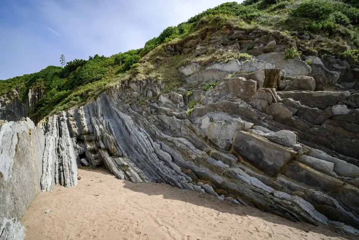 Plage de la côte basque avec falaises rocheuses, surfeurs lointains et eaux calmes