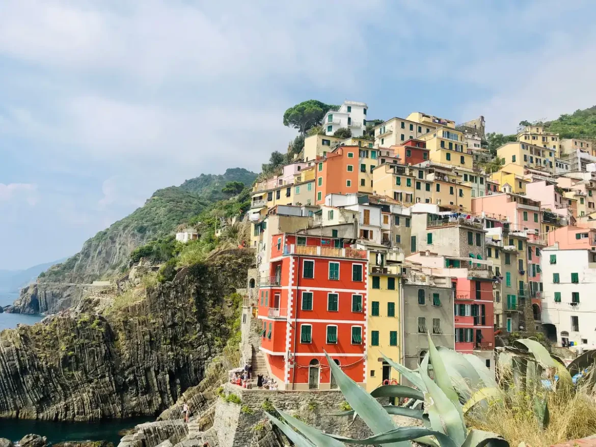 Village côtier ligure aux maisons colorées surplombant la mer, avec terrasses d'oliviers et voie ferrée en bord de côte