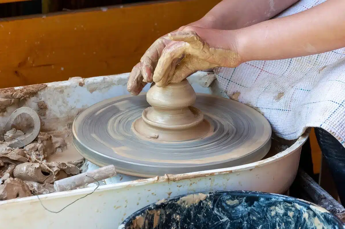 Atelier de céramique avec mains modelant de la terre et pièces en grès sur l'établi
