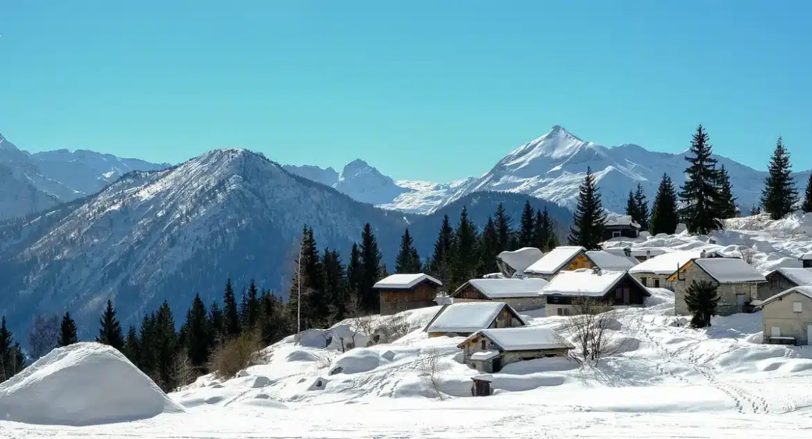 Place de village alpin en journée avec chalets et skis appuyés près d'un local à matériel