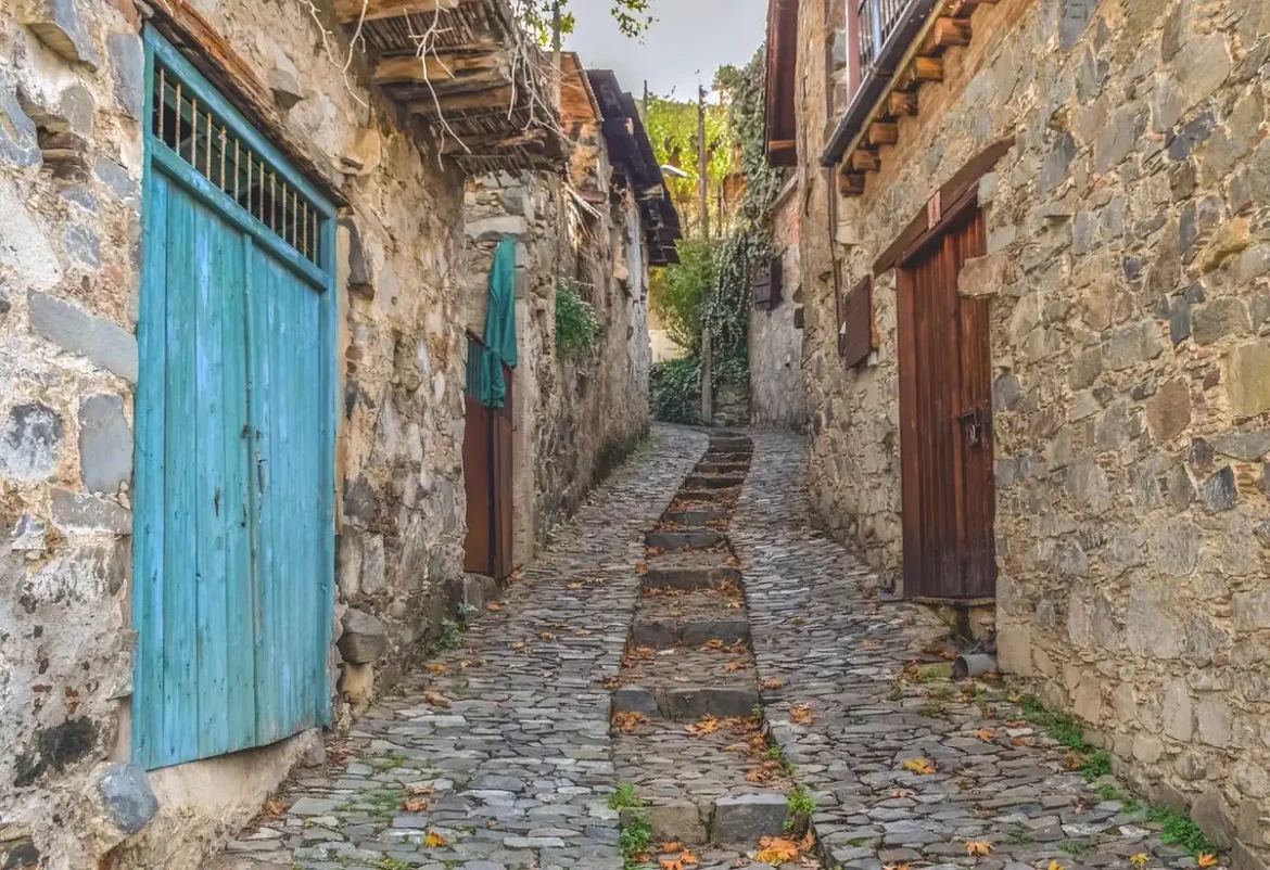 Rue de village en pierre, place avec platanes et collines de châtaigniers au loin