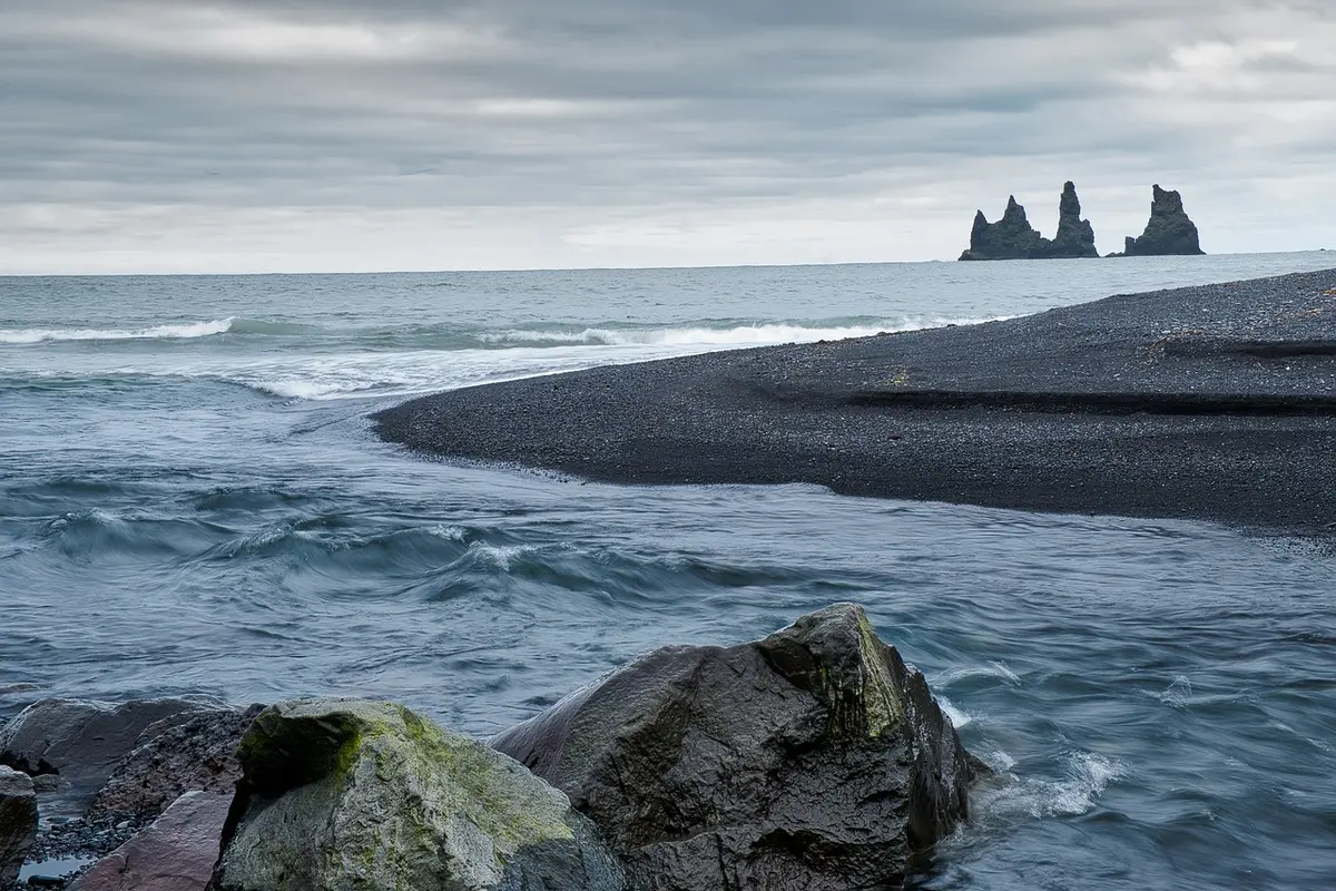 Plage de galets noirs au pied de falaises avec mer turquoise